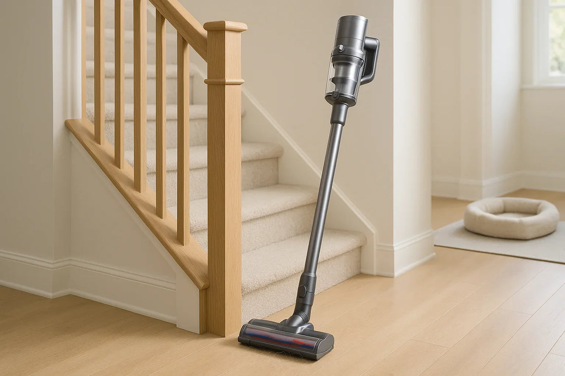 Modern cordless stick vacuum standing upright at the base of a clean staircase with carpeted and hard floor steps showing pet hair near the nozzle