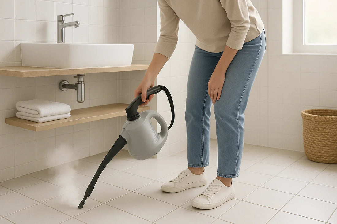 Adult woman using a handheld steam cleaner on grout between floor tiles in a bright modern bathroom with white and pale gray ceramic tiles
